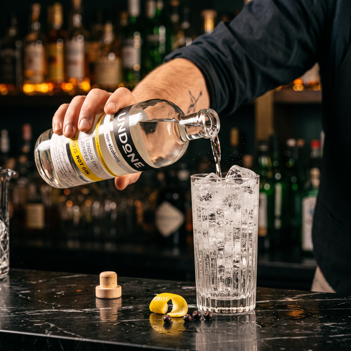 Bartender pouring UNDONE No. 2 NOT GIN into a highball with ice at a dark cocktail bar